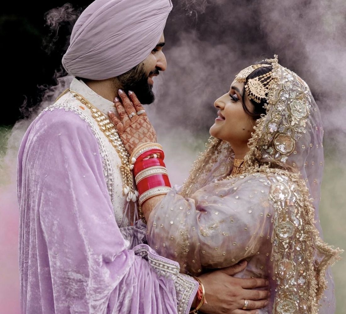 Sikh bride in lilac and gold, smiling at her groom